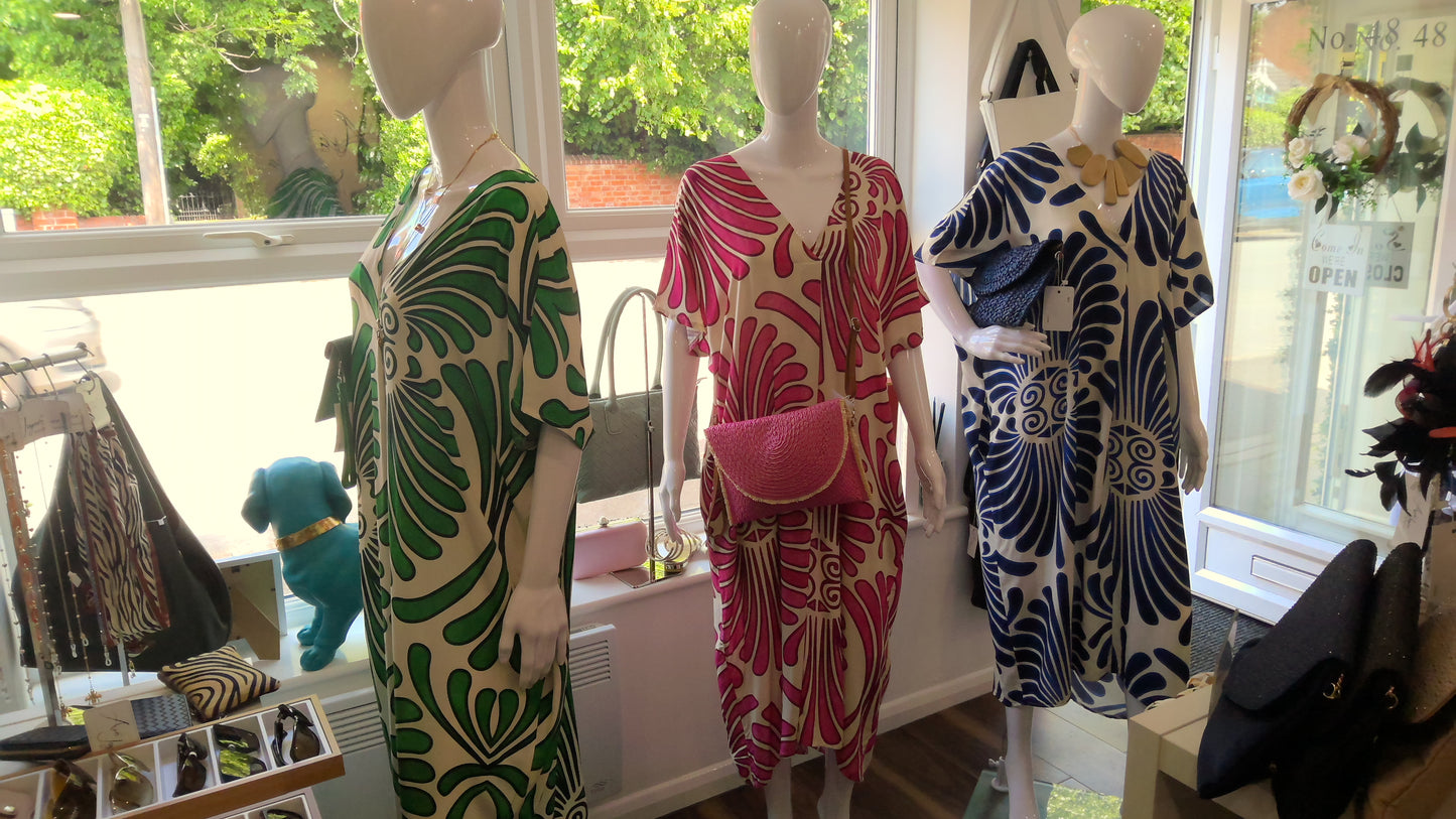 Three mannequins wearing abstract patterned dresses in a store setting with windows.